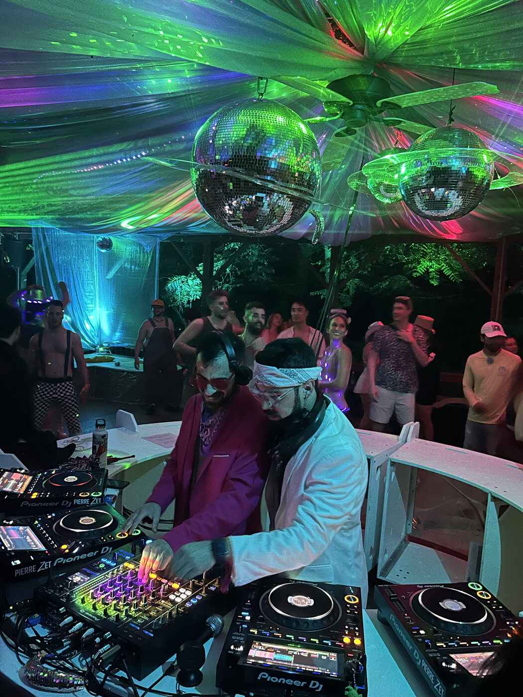 A DJ at the controls inside the 360° round booth, mirror balls and green lasers overhead