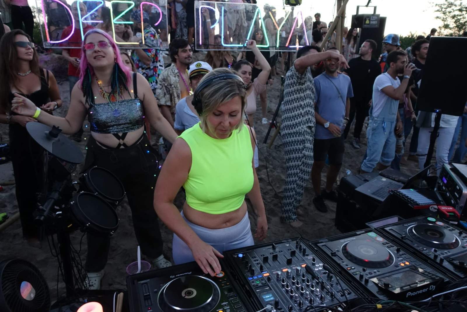 Daniela DJing on the beach at Deep Playa, dancers around the booth and a neon Deep Playa sign behind