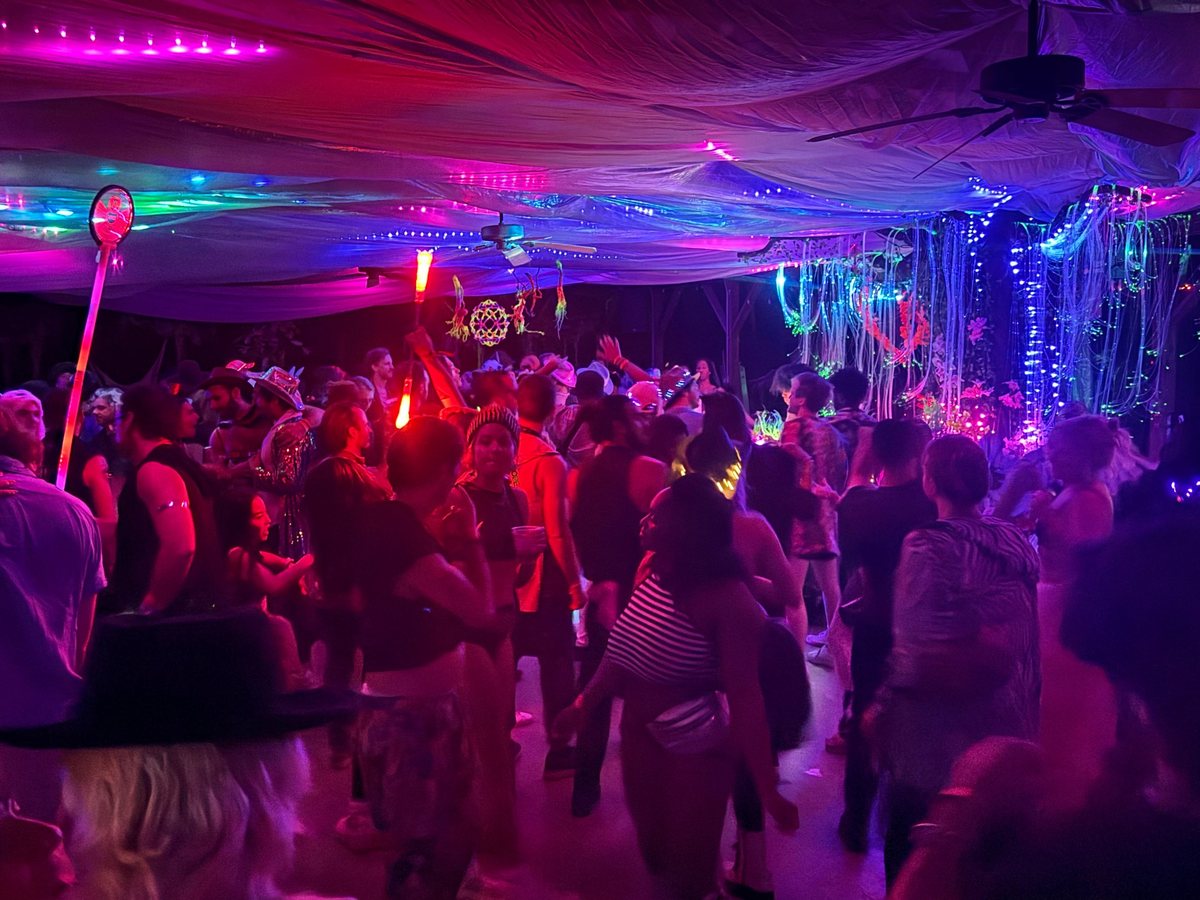 A packed dance floor at the Pavilion under draped fabric and pink light, fiber optics glowing at the far end