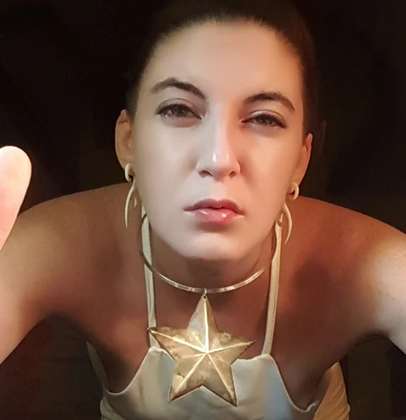 Rhiannon Catalyst in a gold star collar, hands raised toward the camera